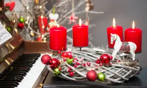 Wieniec adwentowy z czterema czerwonymi świecami i ozdobami, obok fortepianu. Idealny do śpiewania pieśni na adwent.