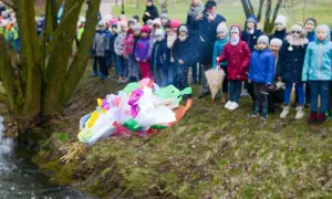 Dzieci obserwują topienie Marzanny, symboliczne pożegnanie zimy. Kolorowa kukła leci do wody.