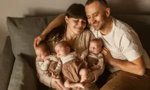Szczęśliwa sesja noworodkowa z rodzicami tulącymi czworo śpiących dzieci.
