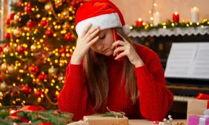 Smutna dziewczyna w czapce Mikołaja rozmawia przez telefon w Wigilię. W tle choinka i świece.