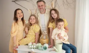 Wesoła sesja pokoleniowa z rodziną w żółtych strojach i króliczymi uszami. Dzieci trzymają ozdoby, a na stole wielkanocne dekoracje.
