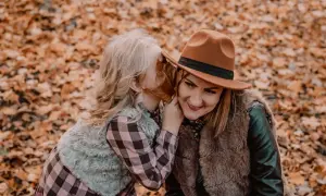 Córka szepcze mamie sekret do ucha podczas sesji mama córka wśród jesiennych liści.
