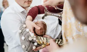 Chrzest dziecka podczas chrzcin. Woda z ozdobnego dzbanka spływa na główkę niemowlęcia.
