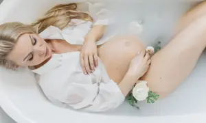 Kobieta w białej koszuli w wannie z kwiatami. Piękna sesja ciążowa, w którym tygodniu?