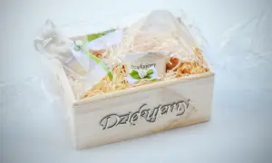Drewniana skrzynka z napisem "Dziękujemy", wypełniona siankiem, zawiera filiżankę z napisem "Dziękujemy" i ozdobne wstążki. Idealny tekst podziękowania dla księdza.
