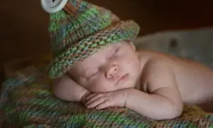 Urocza sesja z dzieckiem. Maluch śpi w czapce zrobionej na drutach, otulony kolorowym kocykiem.