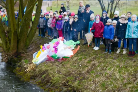 Dzieci obserwują topienie Marzanny, symboliczne pożegnanie zimy. Kolorowa kukła leci do wody.