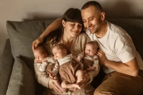 Szczęśliwa sesja noworodkowa z rodzicami tulącymi czworo śpiących dzieci.
