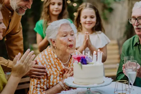 Babcia zdmuchuje świeczki na torcie, rodzina składa życzenia na 51 urodziny.