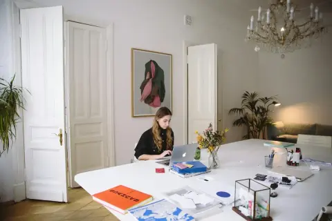 Młoda kobieta pracuje przy laptopie w jasnym pokoju. Czy Wielki Czwartek to święto? Zastanawia się, przeglądając notatki.
