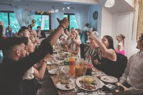 Radosne chrzciny w domu. Rodzina wznosi toasty przy suto zastawionym stole, świętując ważne wydarzenie.