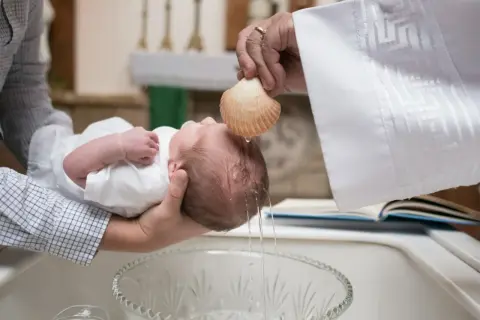 Chrzest dziecka, woda spływa z muszli na główkę. Pytanie, czy chrzestni mogą być tej samej płci, jest tu nieistotne.
