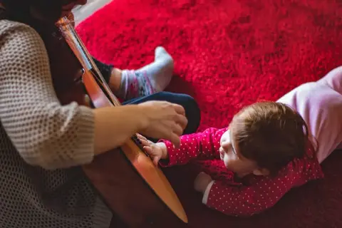 Dziecko słucha piosenek do prezentacji zdjęć z dzieciństwa, gdy ktoś gra na gitarze.