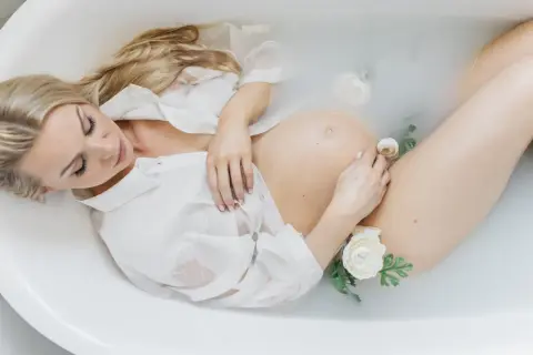 Kobieta w białej koszuli w wannie z kwiatami. Piękna sesja ciążowa, w którym tygodniu?