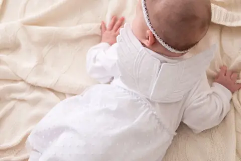 Uroczy niemowlak w białym stroju aniołka, idealny na chrzest. Matka chrzestna znajdzie tu inspirację, co potrzebne do chrztu.