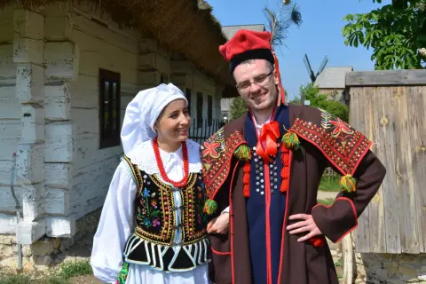Para w tradycyjnych strojach krakowiak, gotowa do tańca. Ona w białej chustce i korale, on w czerwonej czapce z pawim piórem.