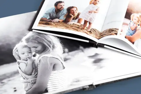 Otwarta fotoksiążka i fotoalbum prezentują rodzinne chwile: mama z dzieckiem na czarno-białym zdjęciu i rodzice z córką na plaży.