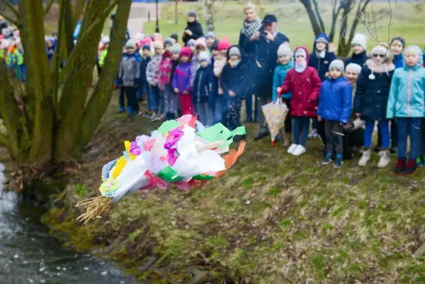 Dzieci obserwują topienie Marzanny, symboliczne pożegnanie zimy. Kolorowa kukła leci do wody.